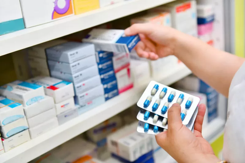 A pharmacist in a pharmacy drugstore holding a box of antibiotics and a capsule pack for treating gonorrhoea