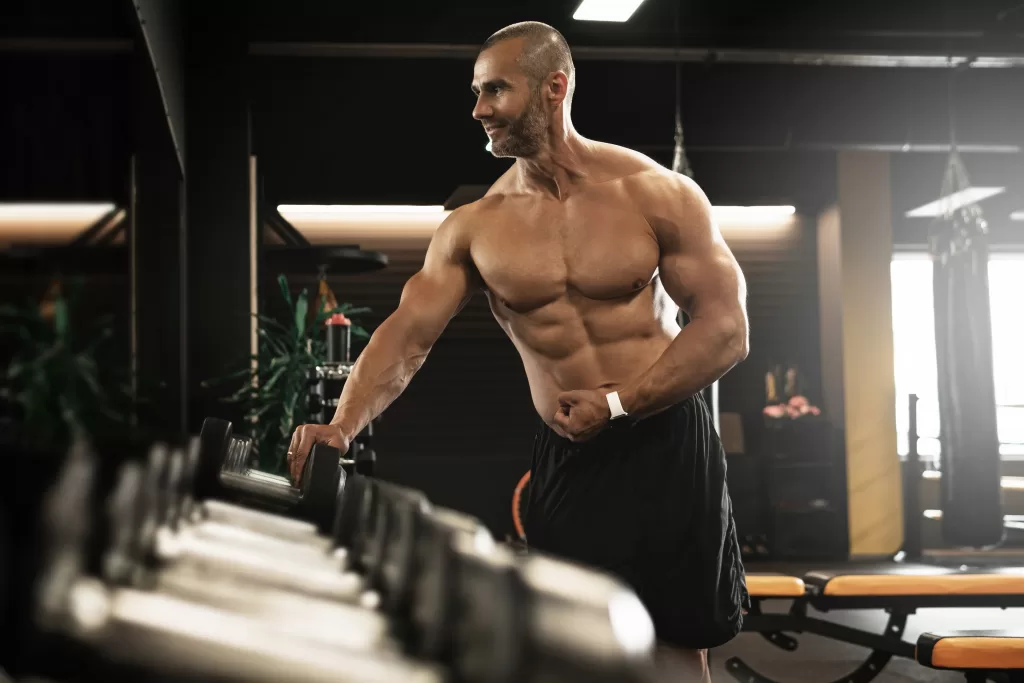 Muscular bodybuilder suffering from bigorexia checking himself in the mirror at the gym