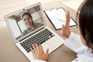 Sick girl wrapped in scarf holding tissue at face and consulting doctor online on video call